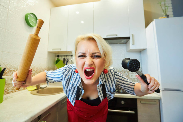 Una chica ama de casa en la cocina con un martillo para golpear la carne. La emoción de la ira. - Foto, Imagen
