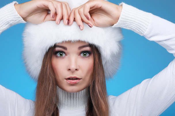 Beautiful merry sexual girl in a white fur cap and warm clothes on a blue background - Фото, изображение