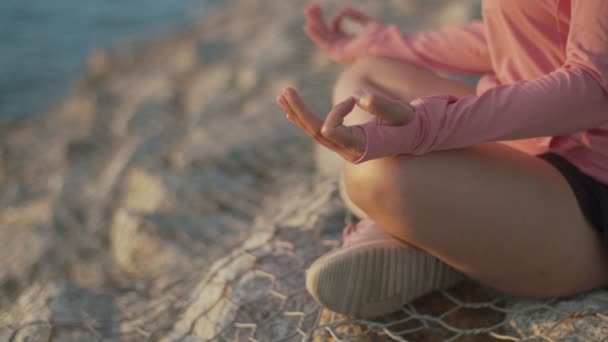 Close up handen Aziatische atletische vrouw mediteren zitten op stenen zee, terwijl prachtige zonsondergang. Zen yoga meditatie praktijk in de natuur. - Video