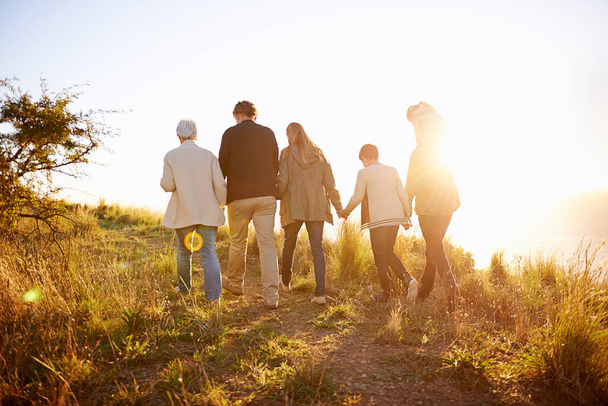 Strolling on a golden afternoon. Rearview shot of a multi-generational family walking together at sunset. - Foto, Bild