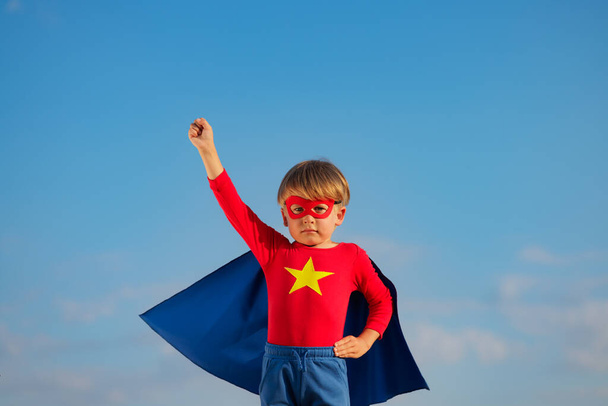 Superhero child playing outdoor. Super hero kid against blue summer sky background. Imagination and freedom concept - Foto, imagen