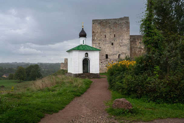 Vista de la Capilla de la Korsunskaya Icono de la Madre de Dios sobre el fondo de la Torre Talavskaya y la pared de la fortaleza de Izborsk en un día de verano, Izborsk, región de Pskov - Foto, Imagen