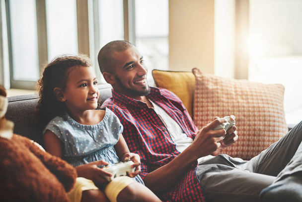 Победитель получает мороженое. Съемка очаровательной маленькой девочки и ее отца, играющих в видеоигры вместе на диване дома. - Фото, изображение