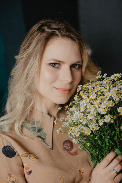 Young blondi pretty woman with bouquet of flowers camomile - Fotografie, Obrázek