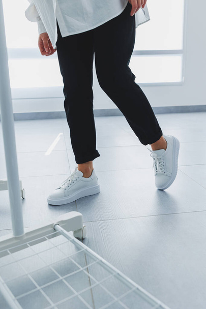 Женские ноги в черных брюках и белых кожаных кроссовках. Современный повседневный стиль. Новая коллекция обуви - Фото, изображение