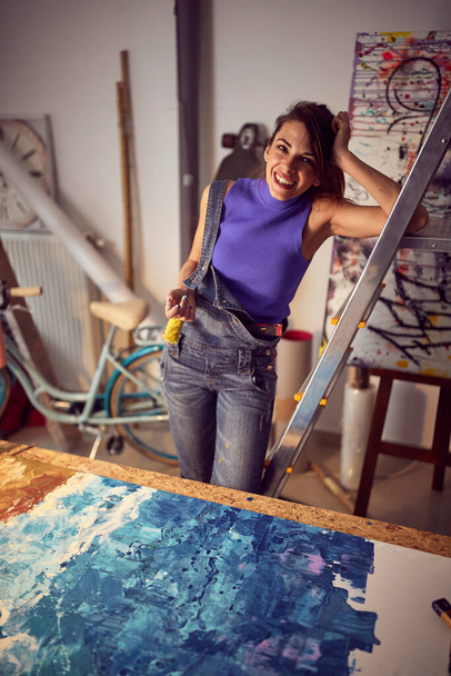 Smiling female drawing on a canvas in art studio.Creative inspired mood. - Фото, зображення