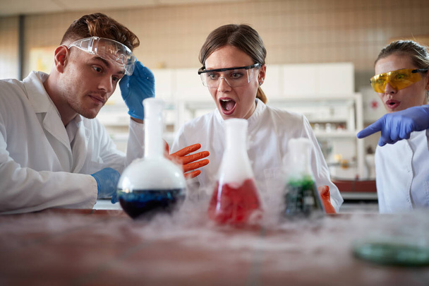 Young chemistry students are astounded by chemical reaction of an experiment in a university laboratory in a working atmosphere. Science, chemistry, lab, people - Photo, image
