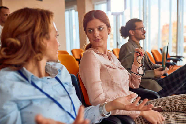 Two female colleagues are chatting during a business lecture in a pleasant atmosphere in the conference room. Business, people, company - Foto, imagen