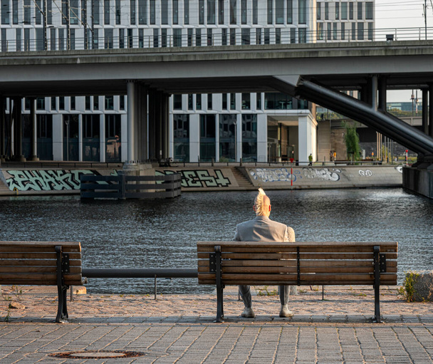 Turyści siedzą nad brzegiem Sprewy w Berlinie i patrzą w kierunku głównego dworca kolejowego, Berlin, Niemcy - Zdjęcie, obraz