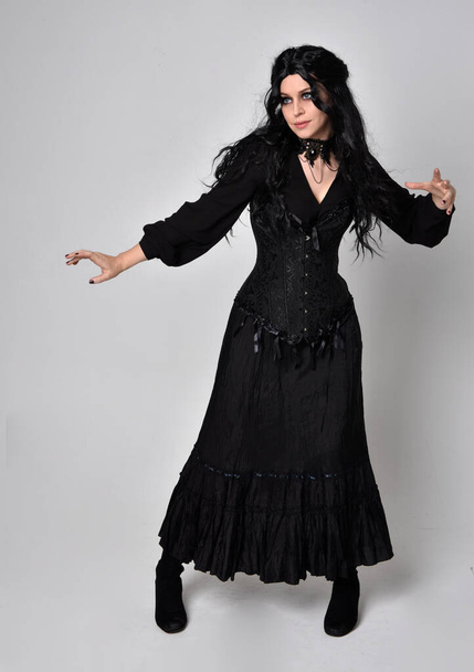 portrait complet de fille aux cheveux roux portant corset noir, robe fantaisie gothique déchiré et bottes en cuir. pose debout, isolé sur fond de studio blanc. - Photo, image