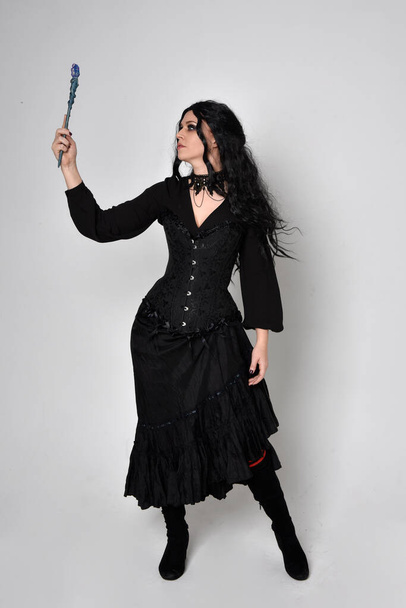 Ganzkörperporträt eines Mädchens mit roten Haaren, das ein schwarzes Korsett, ein zerrissenes Gothic Fantasy Kleid und Lederstiefel trägt. Stehende Pose, isoliert auf weißem Studiohintergrund. - Foto, Bild