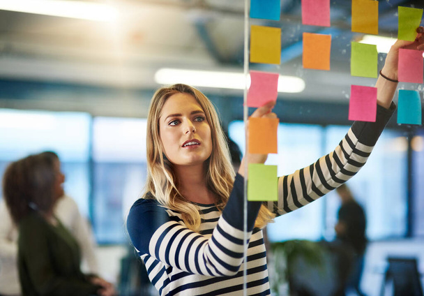 Attaining success with a well mapped out plan. Shot of a young woman having a brainstorming session with sticky notes at work. - Foto, afbeelding