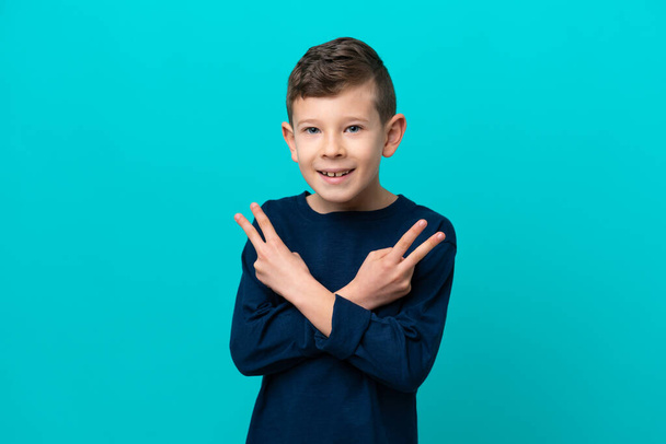 Маленький мальчик на голубом фоне улыбается и показывает знак победы - Фото, изображение
