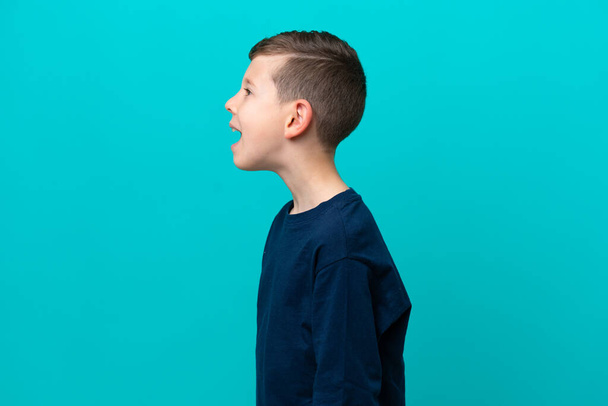 Pieni lapsi poika eristetty sinisellä taustalla nauraa sivusuunnassa - Valokuva, kuva