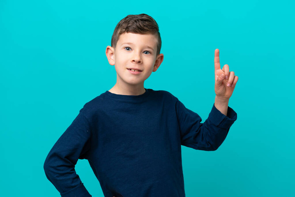 Menino pequeno isolado no fundo azul mostrando e levantando um dedo em sinal do melhor - Foto, Imagem