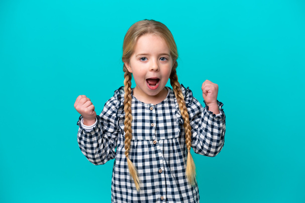 Little caucasian girl isolated on blue background celebrating a victory - Foto, Imagen