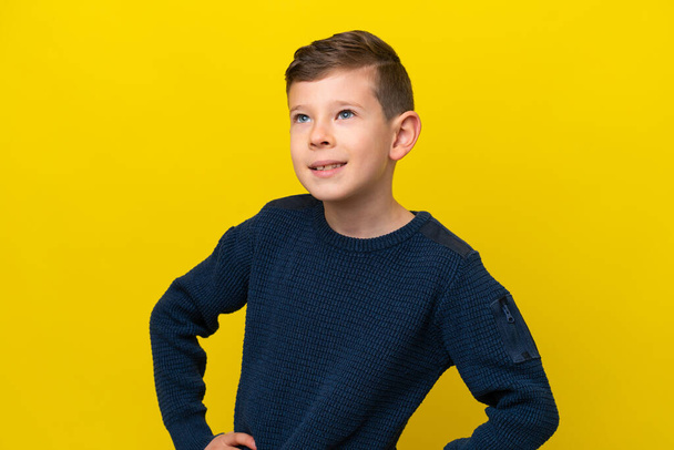 Petit garçon caucasien isolé sur fond jaune posant avec les bras à la hanche et souriant - Photo, image