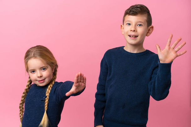 Little caucasian brothers isolated on pink background saluting with hand with happy expression - Foto, Bild