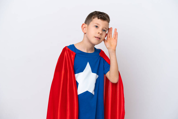 Super Hero маленький мальчик изолирован на белом фоне слушать что-то, положив руку на ухо - Фото, изображение