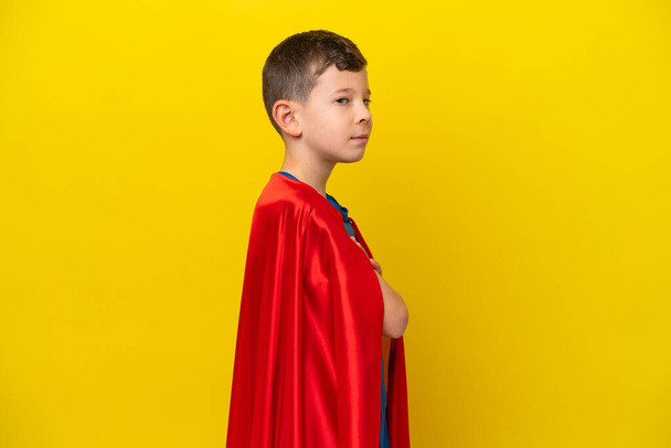 Kleine blanke jongen geïsoleerd op gele achtergrond in superheld kostuum met gekruiste armen - Foto, afbeelding