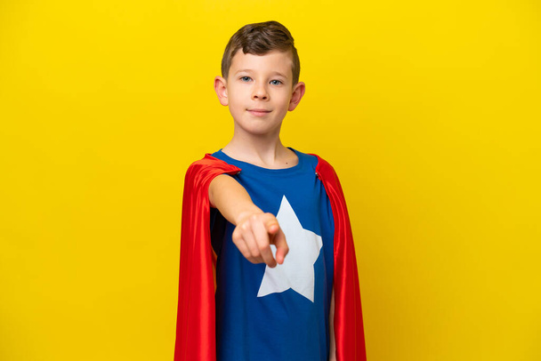 Маленький белый мальчик, изолированный на желтом фоне в костюме супергероя и указывающий на фронт - Фото, изображение