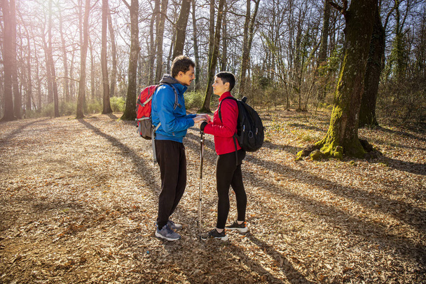 Krásný mladý pár je na túře v lese. Muž o ní mluví s dívkou, když ji bere za ruce. Cestovní a přírodní koncept. - Fotografie, Obrázek