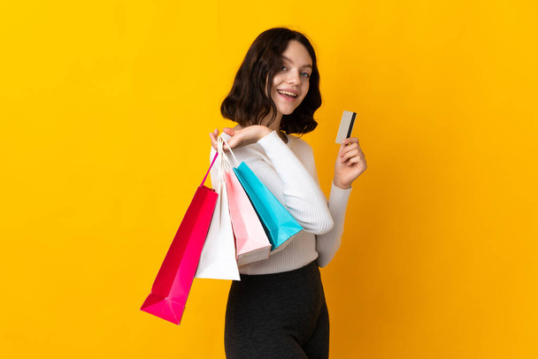 Teenager Ukrainian girl isolated on yellow background holding shopping bags and a credit card - 写真・画像