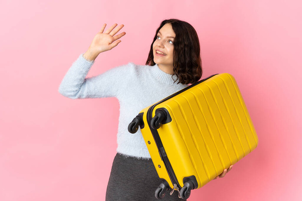 Adolescente ucraniano chica aislado en rosa fondo en vacaciones con viaje maleta y saludo - Foto, imagen