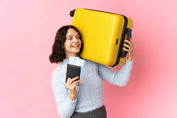 Teenager Ukrainian girl isolated on pink background in vacation with suitcase and passport - Foto, imagen