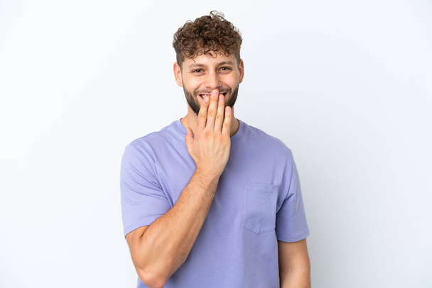 Fiatal jóképű kaukázusi férfi elszigetelt fehér háttér boldog és mosolygós fedő száj kézzel - Fotó, kép