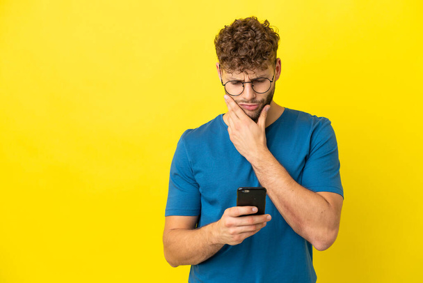 Young handsome caucasian man isolated on yellow background thinking and sending a message - Photo, Image