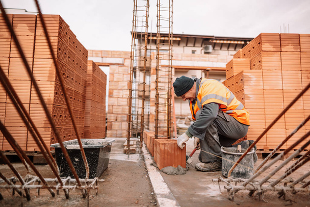 Close up of industrial bricklayer installing bricks on construction site. Construction mason building brick walls - Foto, Imagem
