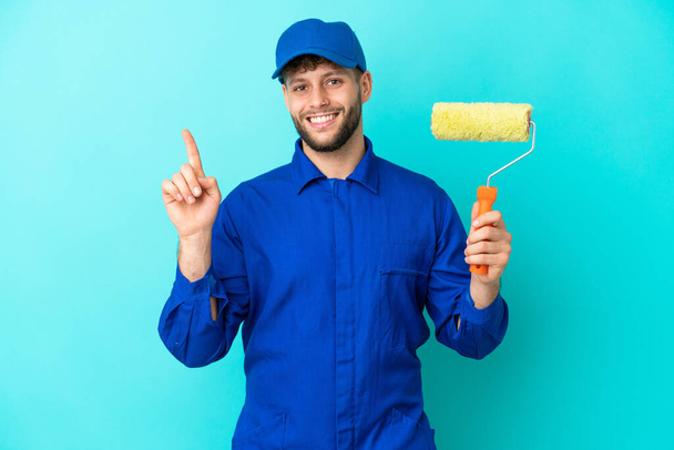 Painter caucasian man isolated on blue background showing and lifting a finger in sign of the best - Foto, Bild