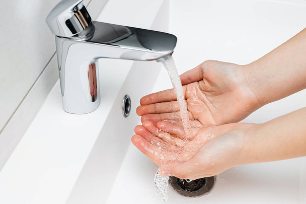Jonge vrouw wassen handen onder stromend water van kraan zonder zeep in de badkamer, hygiëne concept. - Foto, afbeelding