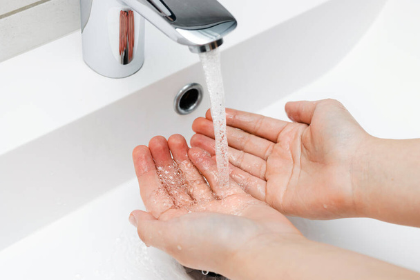 Молодая женщина моет руки под струей воды из крана без мыла в ванной комнате, концепция гигиены. - Фото, изображение