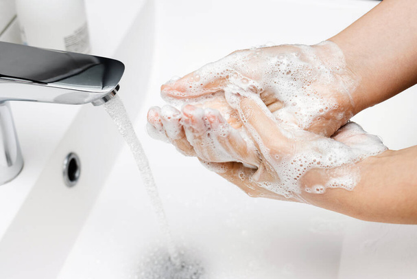 Junge Frau wäscht sich im Badezimmer unter strömendem Wasser aus dem Wasserhahn die Hände mit Seife, Hygienekonzept. - Foto, Bild
