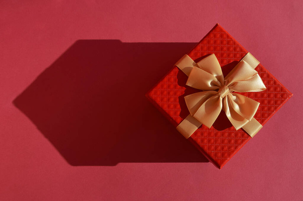 a red gift box with a bow and a shadow in the form of a house on a carmine background. banner for registration. - Foto, imagen