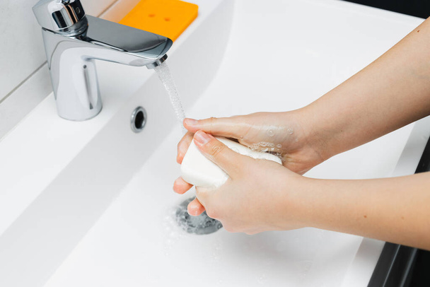Молода жінка миє руки під струменевою водою з крана з милом у ванній кімнаті, концепція гігієни
. - Фото, зображення