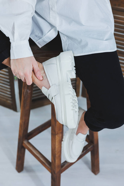 Beine einer jungen schönen Frau in schwarzen Hosen und modernen, stylischen weißen Ledermüßiggängern. Neue Kollektion von Damenschuhen Frühjahr-Sommer 2022 - Foto, Bild