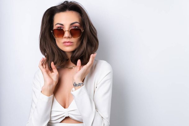Young woman in a cocktail dress, gold chain, bright spring pink makeup on a white background. In fashionable stylish sunglasses. - Foto, Bild
