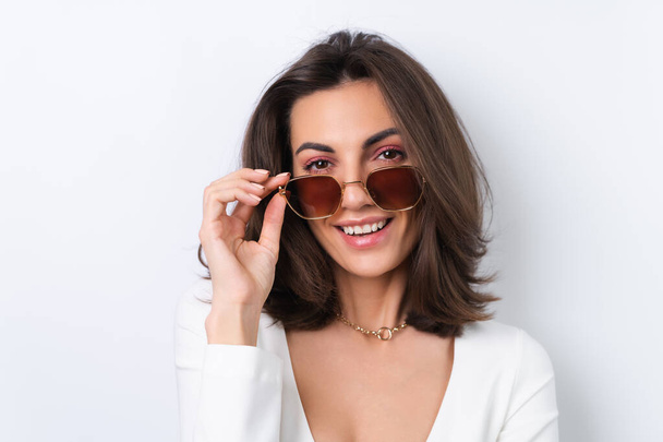 Young woman in a cocktail dress, gold chain, bright spring pink makeup on a white background. In fashionable stylish sunglasses. - Foto, immagini