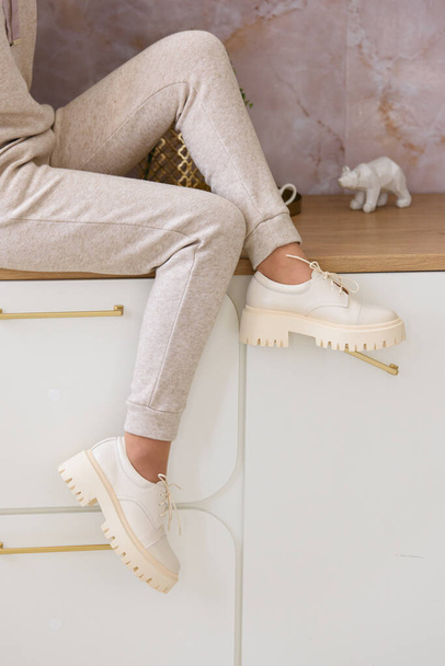 Parte foto di una donna in tuta sportiva beige e scarpe oxford in pelle elegante in posa sulla cucina. focus selettivo - Foto, immagini