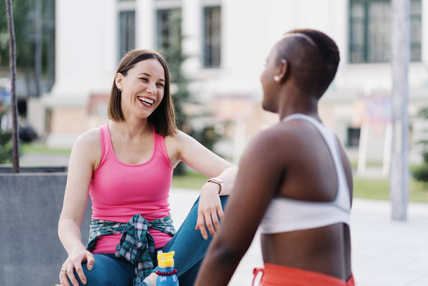 Deux filles courbes multiethniques se détendre après la séance d'exercice, communiquer en plein air. - Photo, image