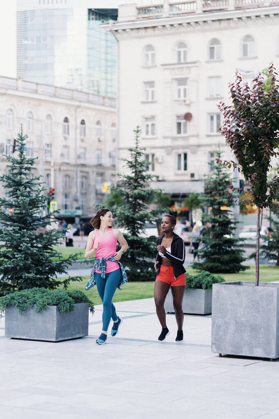 Duas meninas multiétnicas correndo pelas ruas da cidade, comunicando ao ar livre. - Foto, Imagem