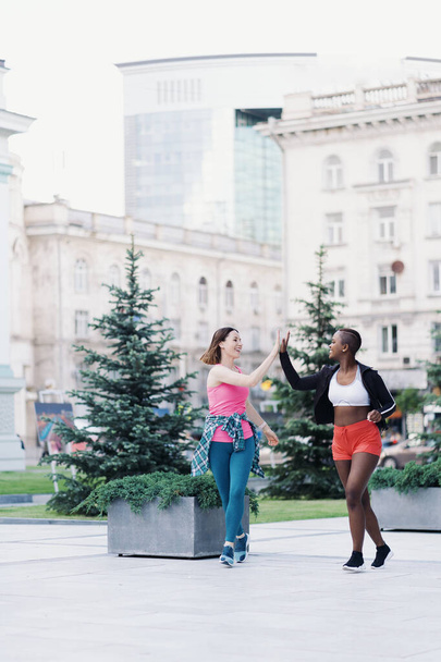 Dwie wielonarodowe dziewczyny biegające po ulicach miasta, porozumiewające się na świeżym powietrzu. - Zdjęcie, obraz