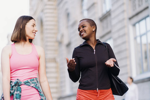Zwei multiethnische Mädchen gehen für eine Übungseinheit, kommunizieren im Freien. - Foto, Bild