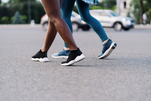 Dos chicas multiétnicas piernas corriendo por las calles de la ciudad, comunicándose al aire libre. - Foto, Imagen