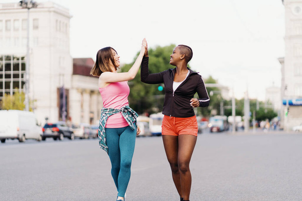Due ragazze multietniche che corrono per le strade della città, comunicando all'aperto. - Foto, immagini