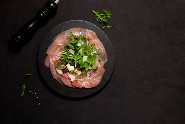 Ιταλικό ορεκτικό κρέατος από λεπτές φέτες ακατέργαστου καπνιστού βοδινού ή γαλοπούλας. Οριζόντια σε μαύρο φόντο, με αντιγραφικό χώρο - Φωτογραφία, εικόνα