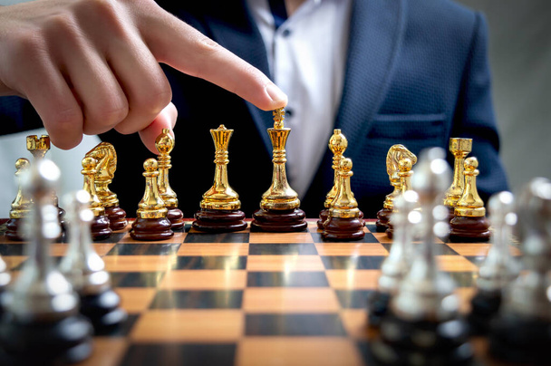 Takım elbiseli bir işadamı satranç oynar. El, altın satranç kralı figürüne dokunarak kazananı gösteriyor. İş stratejisi, beyin fırtınası, takım lideri konsepti. - Fotoğraf, Görsel